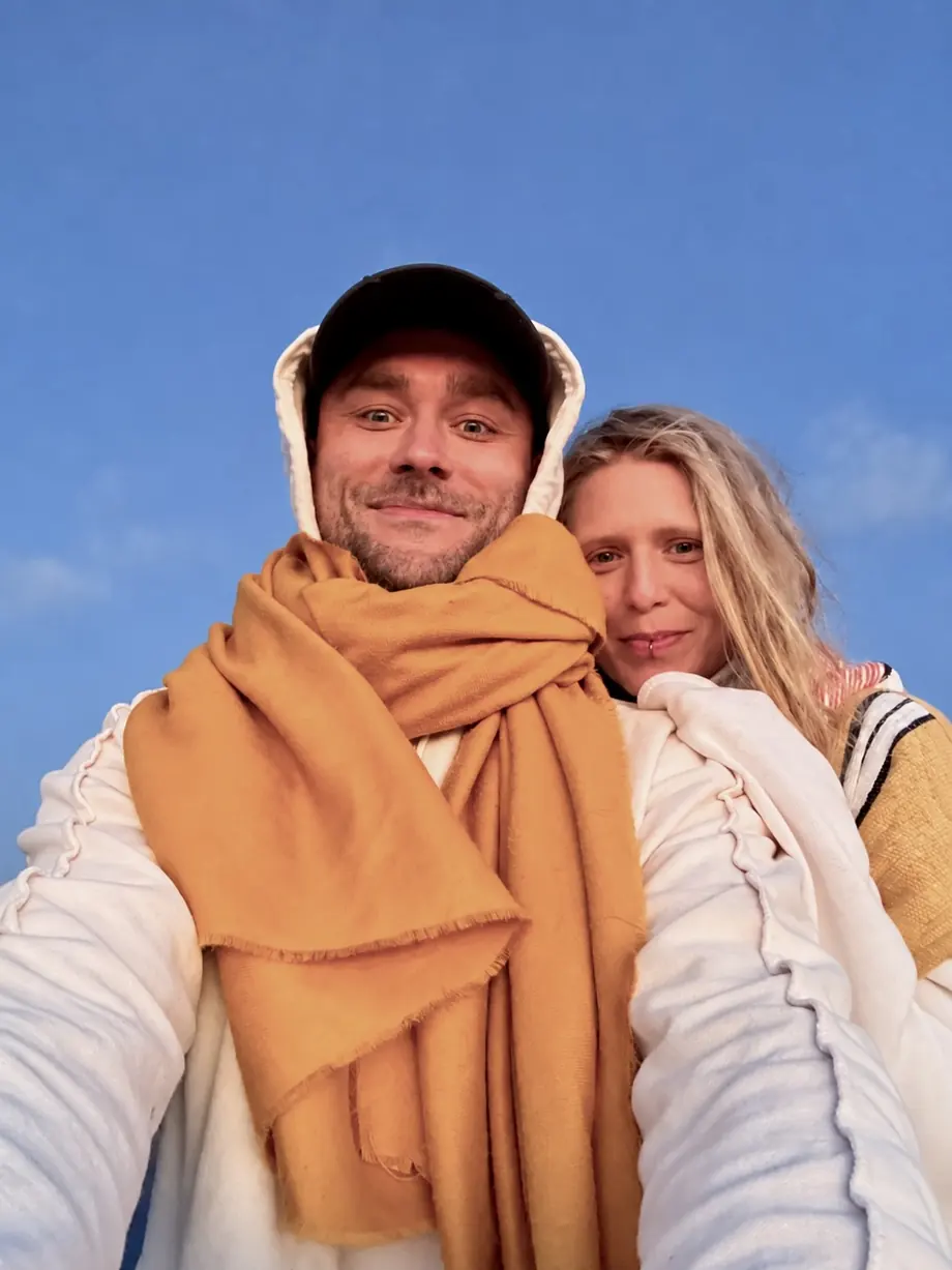 Kuba in a mustard scarf and Mai leaning on his shoulder, blue sky behind them