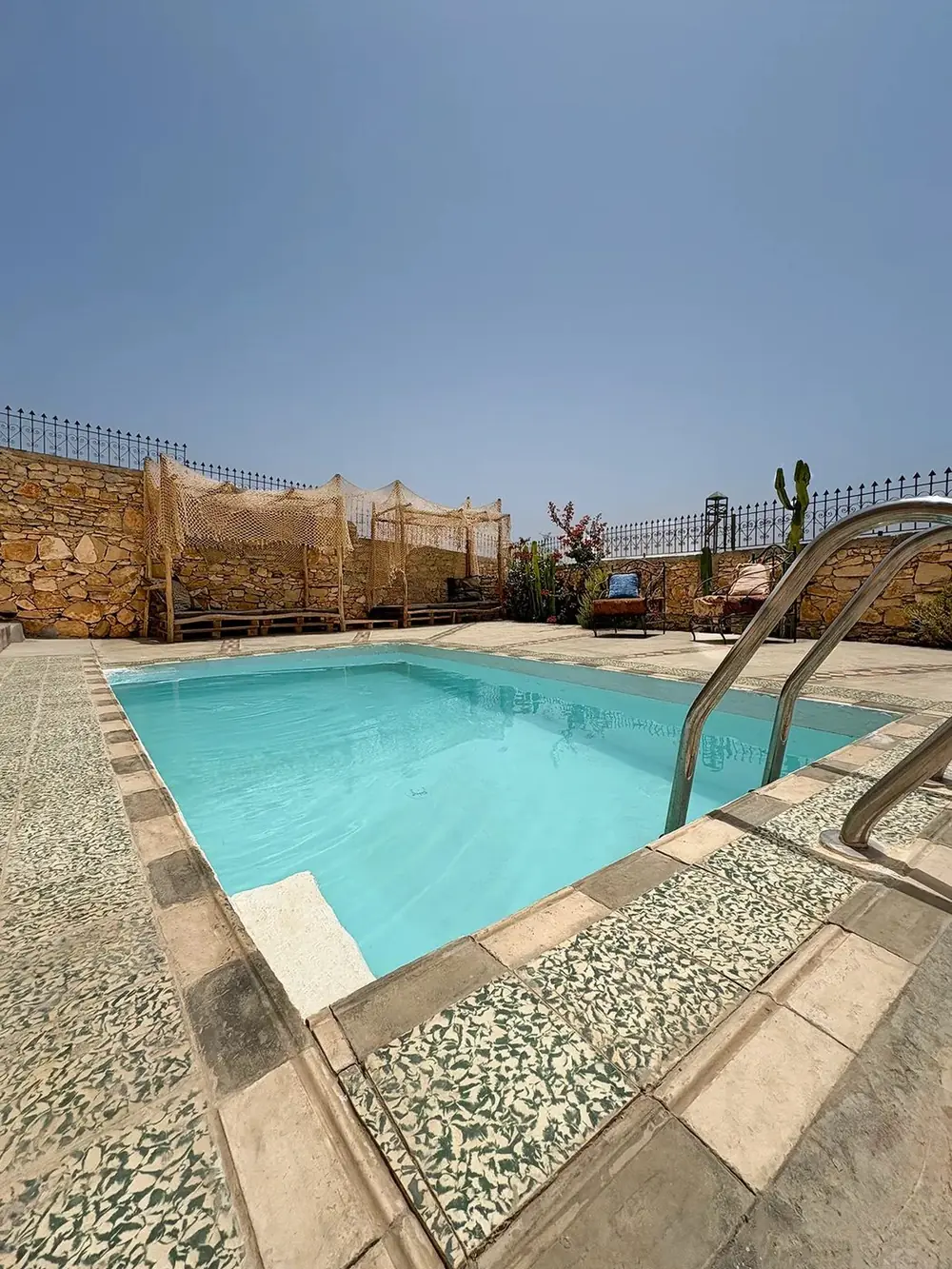 The villa pool with shaded lounge nets along a stone wall
