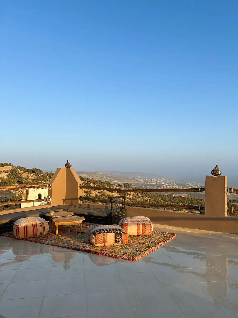 Rooftop lounge with poufs and low tables, hills and coast behind